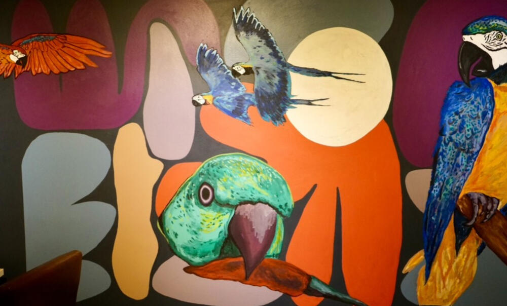 Colorful interior mural featuring tropical birds, bold organic shapes, and a warm geometric background